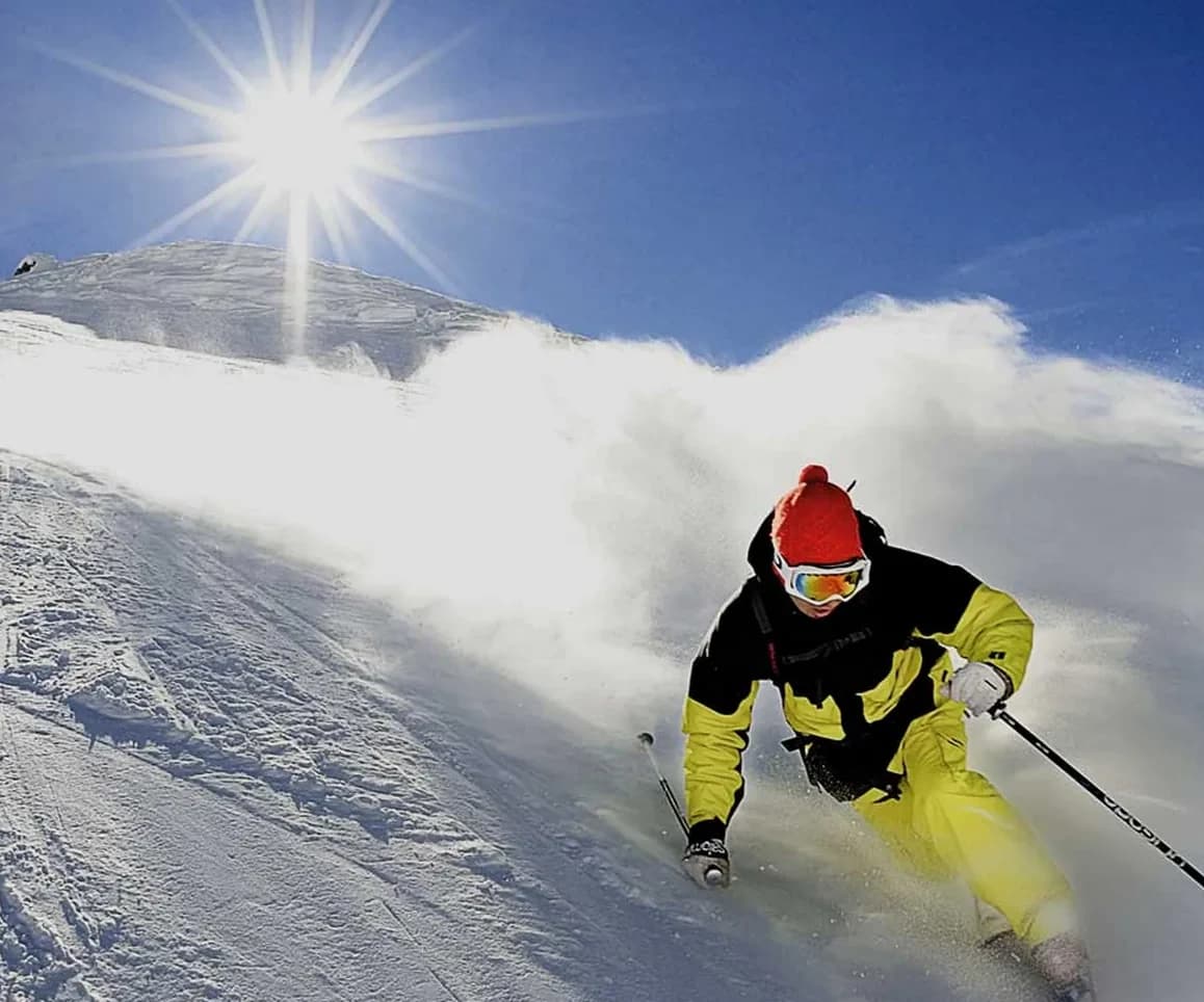 Una curva in neve polverosa controsole, con il sole alto sulla cresta