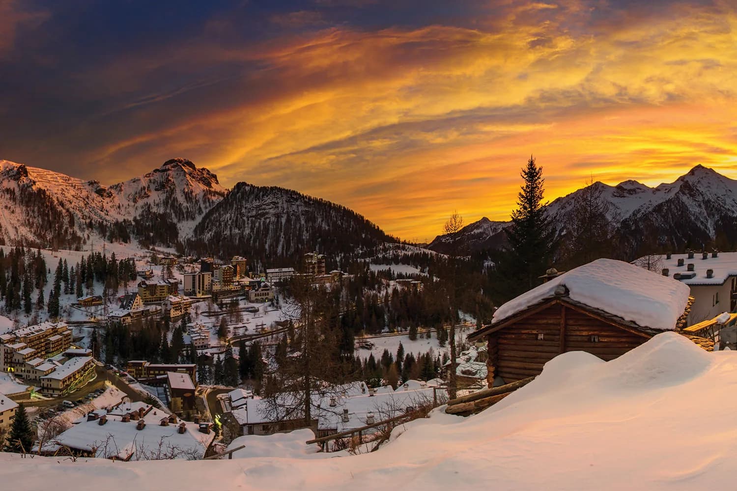 Il paese sotto la neve al tramonto, con il cielo in fiamme sopra le baite